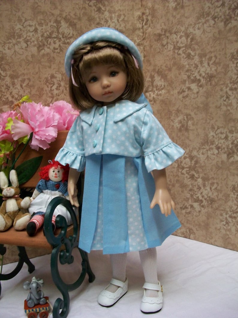 May include: A blue and white polka dot dress with a matching jacket and white hat. The doll is wearing white tights and white shoes. The doll is sitting on a bench with a stuffed animal.