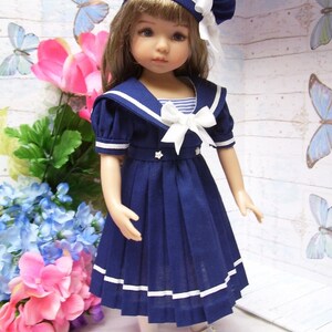 May include: A blue and white sailor dress with a white collar and a white bow. The dress has a pleated skirt and white trim. The doll is wearing a blue and white sailor hat.