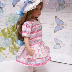 May include: A doll wearing a pink and white striped dress with a white hat decorated with blue and pink flowers. The doll has long brown hair and blue eyes.