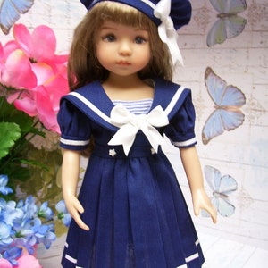 May include: A blue and white sailor dress with a white bow and a blue and white sailor hat. The dress has a pleated skirt and white trim. The doll is wearing the dress and hat.
