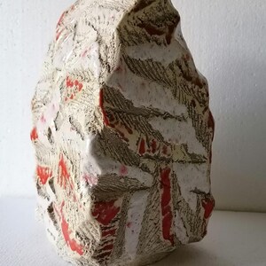 Puede incluir: Escultura abstracta de cerámica con superficie texturizada. La pieza es predominantemente blanquecina, con acentos rojos y marrones. La forma es aproximadamente rectangular con una superficie irregular y dentada, que se asemeja a una roca natural. Una obra de arte decorativa.