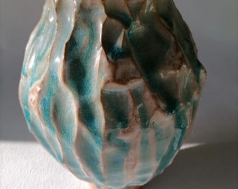 Op de afbeelding: Een keramische pot met een deksel, met een getextureerd, golvend ontwerp in tinten turquoise, bruin en wit.