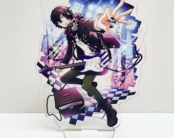 May include: An acrylic stand featuring a cartoon character playing an electric guitar. The character is wearing a black jacket, a white shirt, and black pants. The background is a purple and blue stage with spotlights.