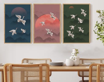 May include: Three framed wall art pieces featuring a Japanese-inspired design. Each piece depicts white cranes in flight against a backdrop of a setting sun and stylized mountains. The color palettes include shades of blue, red, and green.