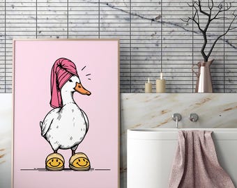 May include: A framed print featuring a cartoon duck wearing a pink towel on its head and yellow smiley face slippers. The duck has an orange beak and is set against a pink background. The artwork is in a bathroom setting.