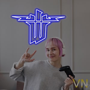 May include: A woman with pink hair wearing headphones and a grey jumper is holding a video game controller. A blue neon sign with a white outline of a stylized letter W with lightning bolts is on the wall behind her.