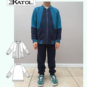 May include: A child's two-tone blue zip-up jacket and navy blue pants. The jacket has a dark blue center panel and sleeves, with a lighter blue body. The child is wearing green sneakers. The image includes the text "EKATOL" and "#Ekatoli129".