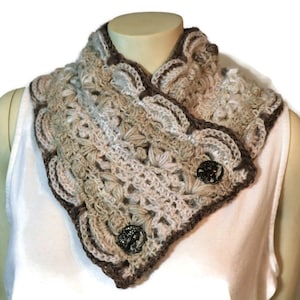 May include: A crocheted cowl with a brown border and two decorative buttons. The cowl is made in a beige and white yarn with a lacy pattern.