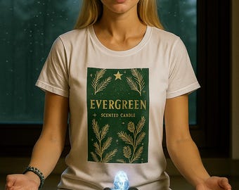 May include: A woman wearing a white t-shirt with the text "EVERGREEN + SCENTED CANDLE" in a green and gold design. She is meditating in a seated position with a small, illuminated fountain in front of her. The background is a window with a view of trees.