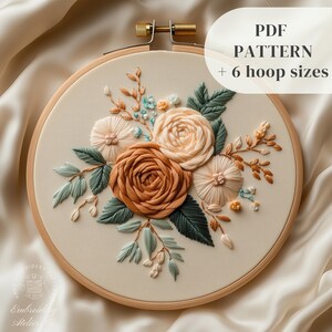 May include: A floral embroidery design in a wooden hoop. The design features a bouquet of flowers in shades of peach, tan, and brown, with green and blue leaves. The text "PDF PATTERN + 6 hoop sizes" is visible.