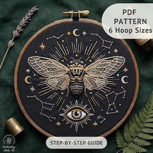 May include: An embroidery hoop containing black fabric with a gold and dark blue cicada design, surrounded by embroidered stars, moons, and constellations. Below the insect is an eye motif. Text reads: PDF PATTERN 6 Hoop Sizes STEP-BY-STEP GUIDE.