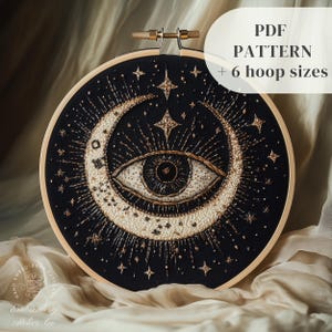 May include: A black embroidery hoop featuring a gold crescent moon and a large eye with a black pupil and gold iris. The eye is surrounded by gold stars and rays of light. The text "PDF PATTERN + 6 hoop sizes" is in the top right corner of the image.