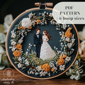 Könnte beinhalten: Stickerei-Bild in einem Stickrahmen mit einem Paar in einem Blumenkranz. Das Paar ist in einem stilisierten, minimalistischen Stil dargestellt, der Bräutigam in einem dunklen Anzug und die Braut in einem weißen Kleid. Der Kranz besteht aus verschiedenen Blumen in Weiß-, Gelb- und Grüntönen. Der Hintergrund ist dunkelblau.