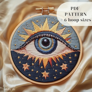 Puede incluir: Ojo bordado con un iris azul y un diseño de sol amarillo sobre un fondo azul oscuro con estrellas doradas. El bordado está en un aro de madera. PATRÓN PDF + 6 tamaños de aro.