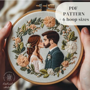Puede incluir: Arte de bordado en aro que presenta a una pareja besándose rodeada de una corona de flores. El aro está hecho de madera y tiene un fondo de tela blanca. El bordado está hecho en tonos de verde, blanco y melocotón. El texto "PDF PATTERN + 6 hoop sizes" es visible en la esquina superior derecha de la imagen.