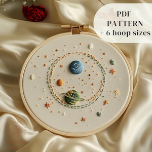 Puede incluir: Un aro de bordado blanco con un diseño de bordado colorido de planetas y estrellas. El texto "PDF PATTERN + 6 hoop sizes" está en la esquina superior derecha de la imagen.