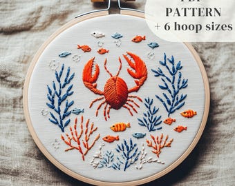 May include: Embroidered hoop art featuring a red crab surrounded by blue and orange coral and fish. The hoop is on a beige fabric background. The text "PDF PATTERN + 6 hoop sizes" is in the upper right corner of the image.