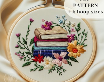 Puede incluir: Primer plano de una pila de libros bordados con flores coloridas que los rodean. Los libros están en un aro de bordado de madera. El texto "PDF PATTERN + 6 hoop sizes" está en la parte superior de la imagen.