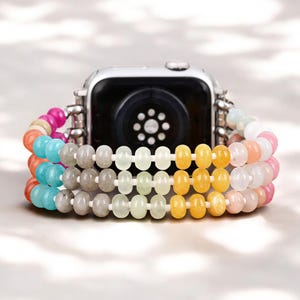 May include: A colorful beaded watch band made of turquoise, yellow, gray, and pink beads. The band is designed to fit a smart watch.