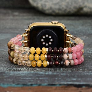 May include: A gold watch band with a multi-colored beaded design. The band features pink, yellow, and brown beads.