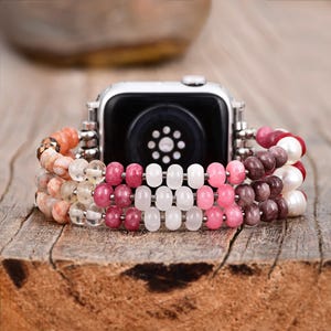 May include: A pink, white and brown beaded watch band with a silver watch face. The band is made of multiple strands of beads, including pink, white and brown beads.