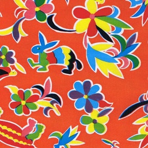 May include: A bright orange fabric with a colorful floral pattern. The pattern includes flowers, leaves, and a rabbit. The flowers are in shades of red, yellow, blue, and green. The leaves are in shades of green and yellow. The rabbit is in shades of blue, green, and yellow.