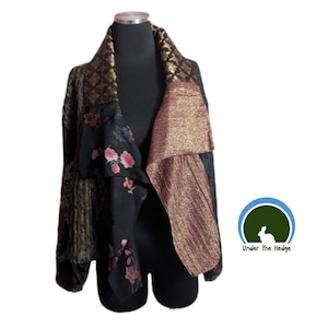 May include: A jacket featuring a patchwork design with a black base, floral patterns in pink and red, and metallic gold textured panels. The garment has a wide lapel and long sleeves, displayed on a mannequin. The logo Under the Hedge is visible.