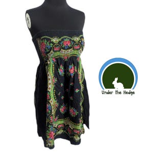 Puede incluir: Vestido negro sin tirantes con estampado floral. La parte superior es fruncida y la falda es holgada. El diseño floral presenta flores rojas, rosas y azules con detalles verdes. El vestido se exhibe en un maniquí negro.