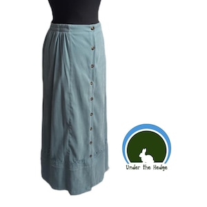 May include: A long, light blue skirt with a button-down front and a decorative hem. The skirt has a high waist and a relaxed fit. The buttons are a dark brown color. The skirt is made of a soft, corduroy-like material.