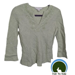 Può includere: Un top a maniche lunghe color verde salvia chiaro con scollo a V caratterizzato da un intricato ricamo di perline argentate attorno al colletto. Il capo presenta un tessuto testurizzato, maniche a tre quarti e piccoli spacchi laterali sull'orlo.
