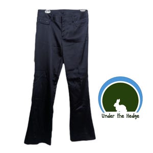 May include: A pair of solid black trousers with a smooth, satin-like finish, featuring a standard waistband with belt loops, a front zipper fly, and two front pockets. Next to the trousers is a circular logo with a rabbit and the text Under the Hedge.