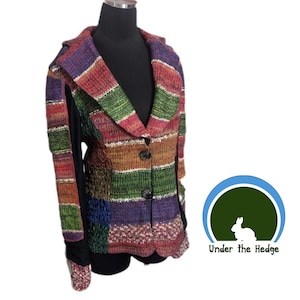 May include: A colorful, striped knit jacket with a collared neckline and three dark buttons. The jacket features a patchwork design with various colors including red, green, purple, and brown. The sleeves are black with a patterned cuff. The logo "Under the Hedge" is in the bottom right.