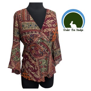 Könnte beinhalten: Ein gemustertes Wickeloberteil mit langen, ausgestellten Ärmeln. Das Oberteil hat einen V-Ausschnitt und eine taillierte Taille. Der Stoff hat ein Paisley-Design in Burgunderrot, Orange, Grün und Beige. Das Logo "Under the Hedge" befindet sich in der oberen rechten Ecke.