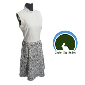 May include: A sleeveless dress featuring a solid cream-colored high-neck bodice and a flared skirt with a black and white geometric pattern. Next to the dress is a circular logo with a white rabbit and the text Under the Hedge.