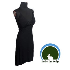 Könnte beinhalten: Ein schwarzes Kleid mit Spaghettiträgern und V-Ausschnitt. Das Kleid hat ein figurbetontes Oberteil und einen leicht ausgestellten Rock. Der Stoff hat subtile Glitzerdetails. Das Kleid wird auf einer schwarzen Schaufensterpuppe präsentiert.