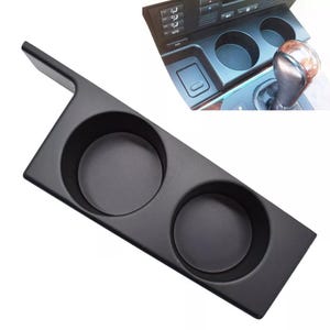 Puede incluir: Portavasos de plástico negro con dos aberturas circulares. El portavasos está diseñado para encajar en la consola central de un automóvil.