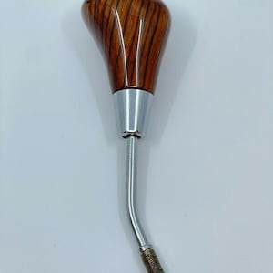 May include: A wooden gear shift knob with a brown and reddish-brown wood grain pattern. The knob has a silver metal base and a long silver metal shaft.