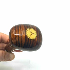May include: A wooden gear shift knob with a gold Mercedes-Benz logo.