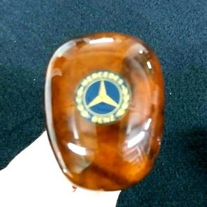 Puede incluir: Una palanca de cambios de madera marrón con un logotipo dorado de Mercedes-Benz.