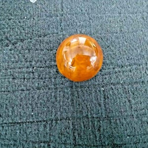 May include: A round, orange, translucent cabochon gemstone with a smooth, polished surface.