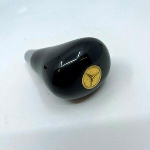 Può includere: Pomello del cambio nero con logo Mercedes-Benz dorato.