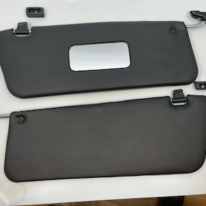 May include: Two black leather car sun visors with a chrome metal frame and a small rectangular mirror on the top visor.