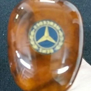 Puede incluir: Un pomo de volante de madera marrón con un logotipo de Mercedes-Benz en oro y azul.