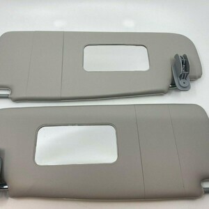 May include: Two gray car sun visors with a rectangular window in each. The visors have a clip on the side to attach to the car.