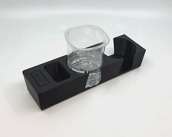May include: A black plastic cup holder with a clear plastic cup inside. The cup holder has a small compartment on the side.