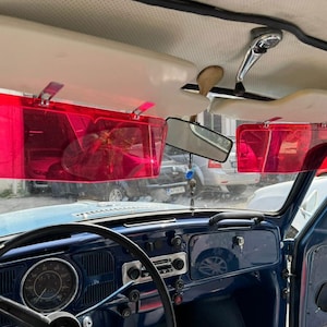 May include: A blue vintage car interior with two pink sun visors installed above the dashboard. The car has a steering wheel, a speedometer, and a radio.
