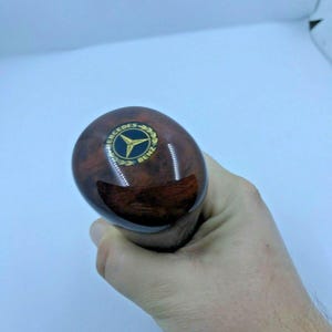Puede incluir: Una palanca de cambios de madera marrón con un logotipo dorado de Mercedes-Benz.