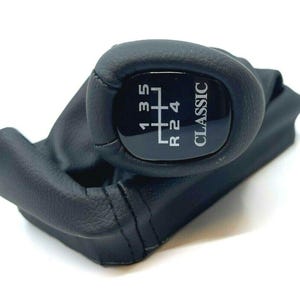 May include: Black leather gear shift knob with a black plastic top. The top has a white gear pattern and the word "CLASSIC" printed on it.
