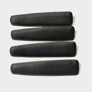 Puede incluir: Cuatro pinzas para el pelo de cuero negro. Las pinzas son todas del mismo tamaño y forma, y tienen una superficie texturizada.