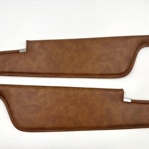 May include: Two brown car sun visors with a textured surface and a metal bracket. The visors are a warm brown color and are designed to block sunlight. The visors are new and ready to install.